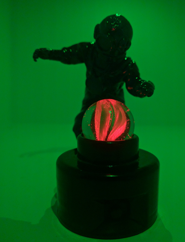 Green-lit figurine with a glowing red orb on a black base.